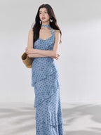 A woman in a light blue polka dot long slip dress with ruffled layers and an adjustable strap.