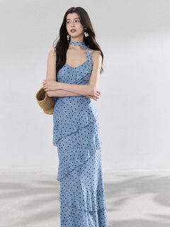 A woman in a light blue polka dot long slip dress with ruffled layers and an adjustable strap.