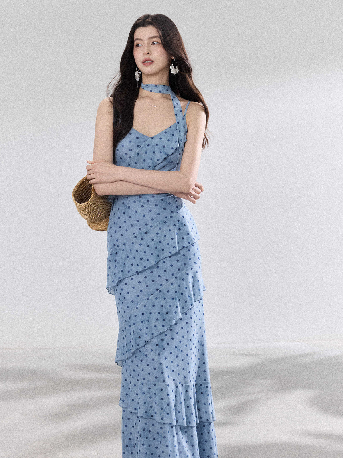 A woman in a light blue polka dot long slip dress with ruffled layers and an adjustable strap.