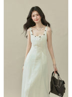 Ivory sleeveless dress with a straight hem, side pockets, and button details on the neckline.