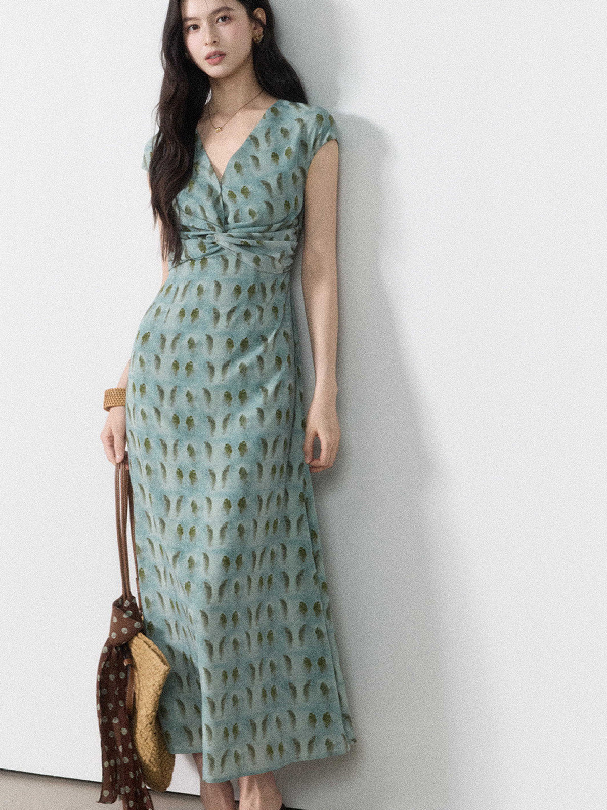 A woman in a long, light blue dress with a green leaf pattern and a twisted knot at the waist.