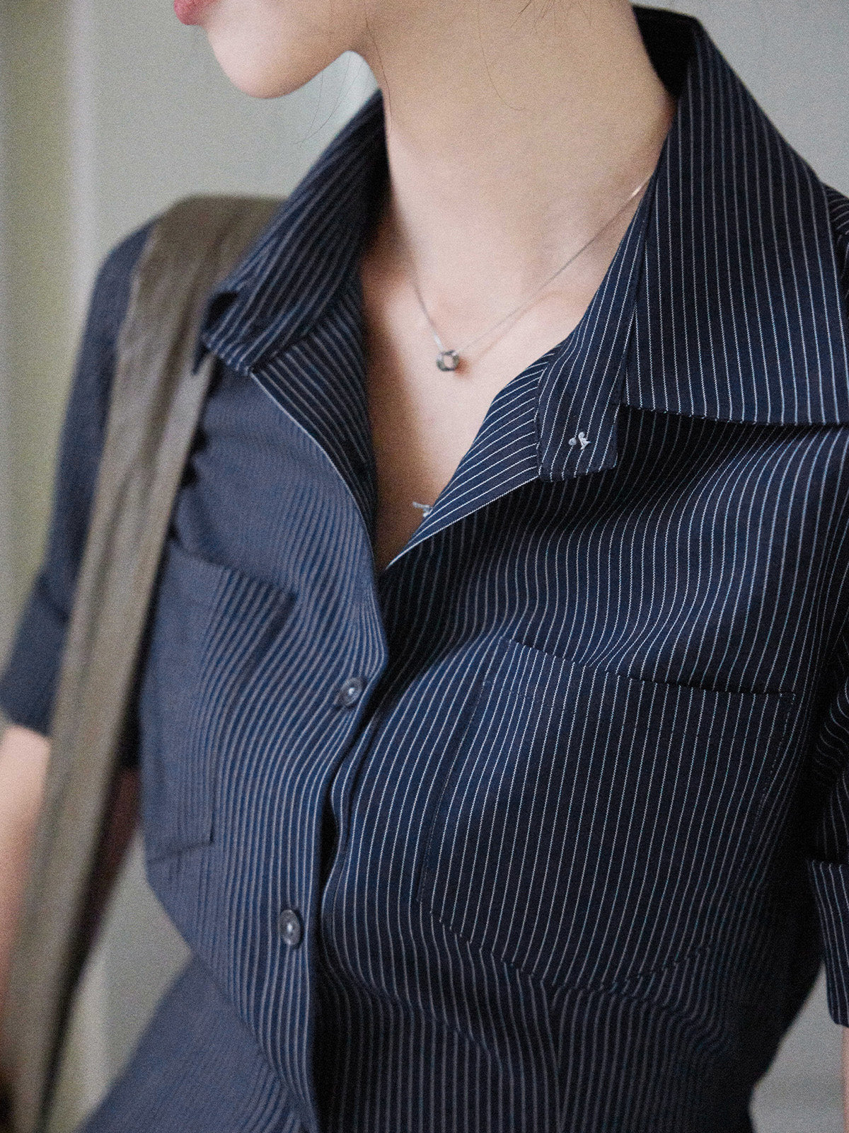 A close-up of the neckline and chest pocket of a navy striped fitted top with a collar, button-front closure, and cuffed sleeves.