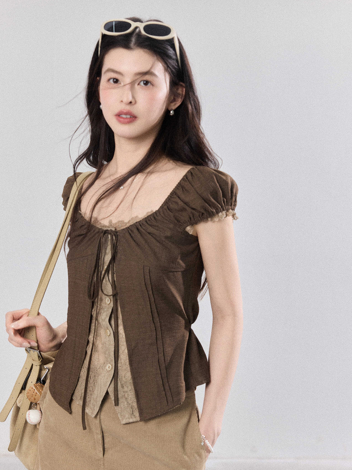 Model wearing a brown puff sleeve top with sunglasses and a beige bag.